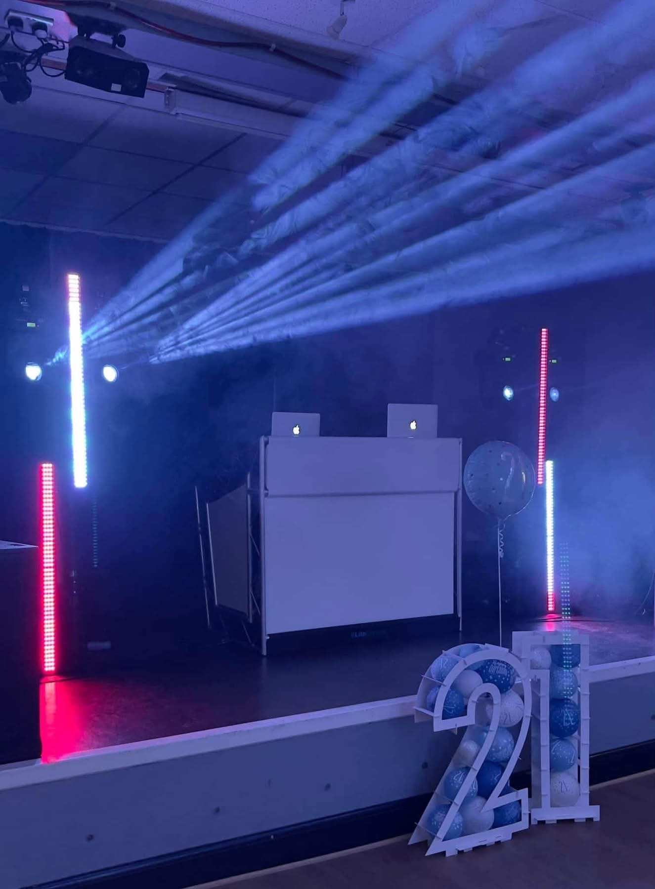 21st birthday party set-up with LED battens, haze and blue aerial beams over a white DJ booth