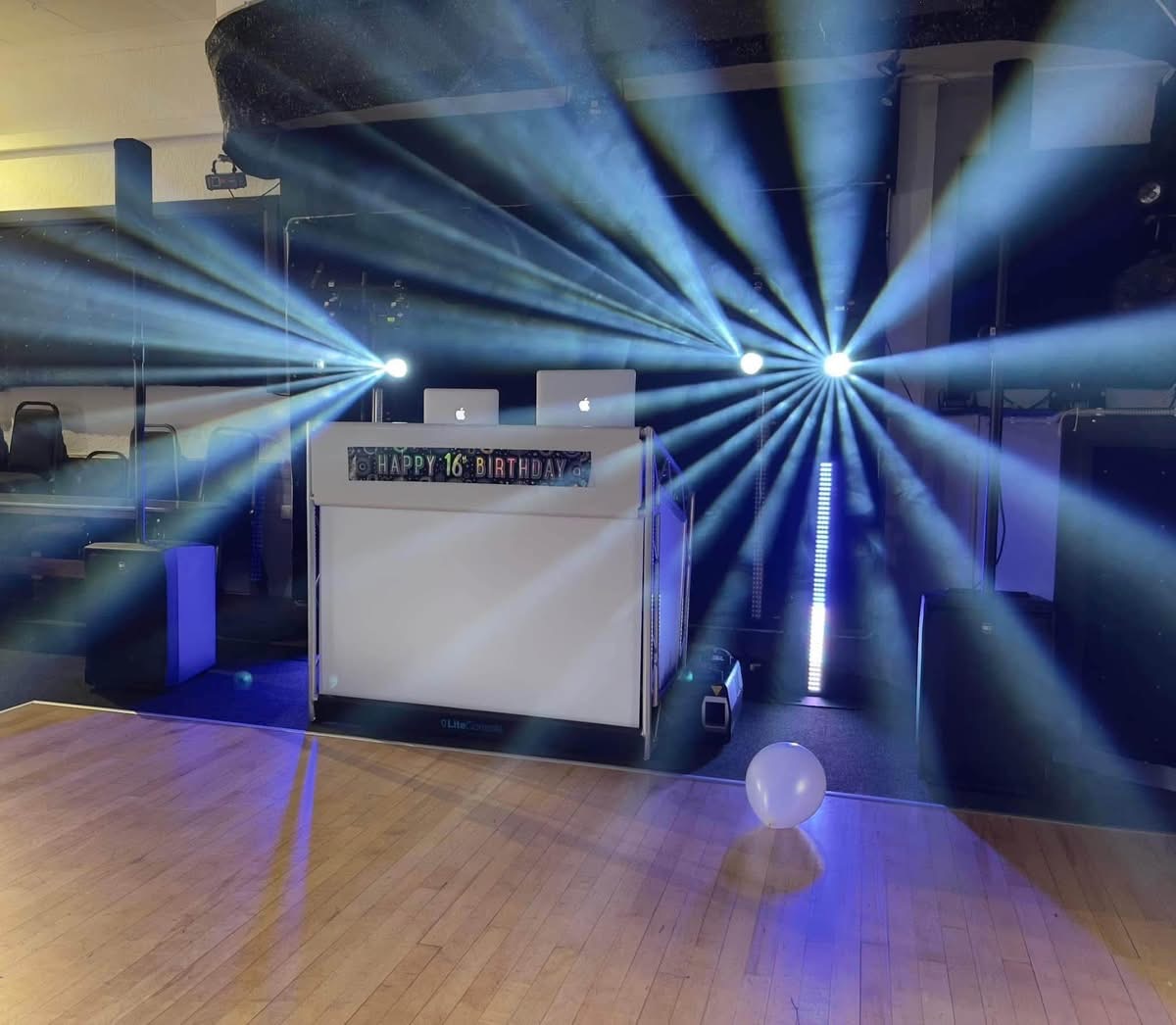 White DJ booth with blue beam lighting fanning across a birthday party dance floor