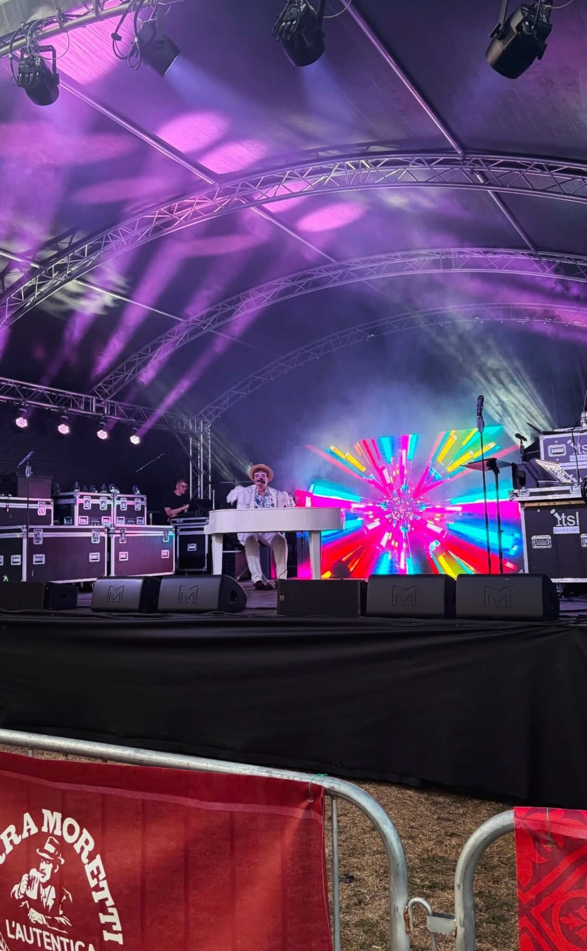 Festival main stage with purple moving-head beams, LED video wall and stage monitors during a live piano set